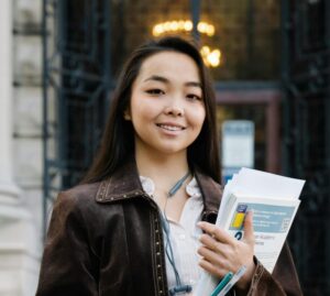 Confident female student holding papers in front of an ornate historic building.